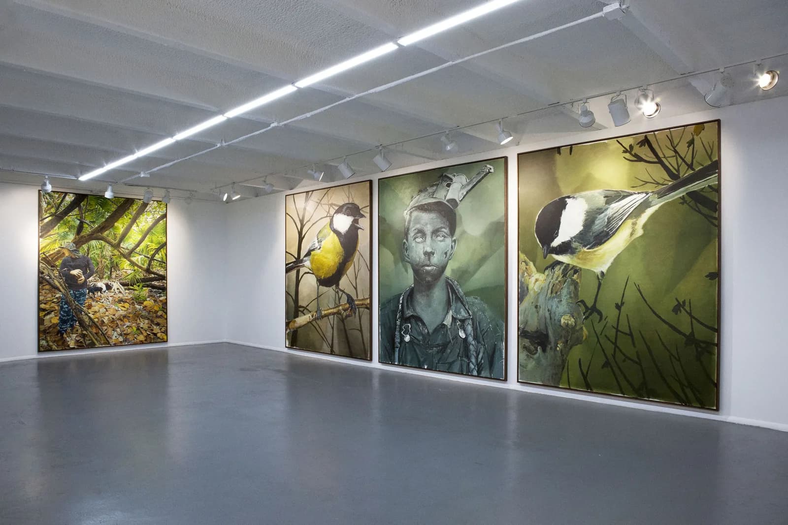 Sala de la galería con un tríptico de un pájaro, un niño con gorra y otro pájaro, y una pintura vertical de una figura en el bosque en la pared del fondo.